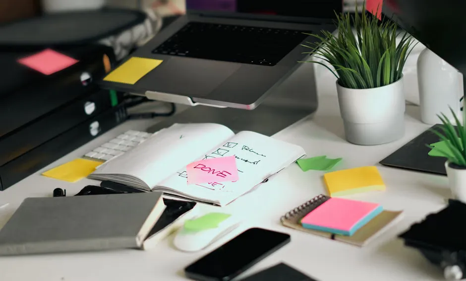 A laptop and a printed checklist on a kitchen table in daylight, a pen resting on the list, no person in frame
